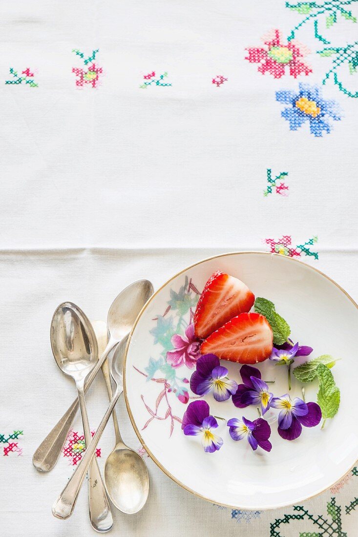 Frische Erdbeeren, Hornveilchen und Minze auf Teller