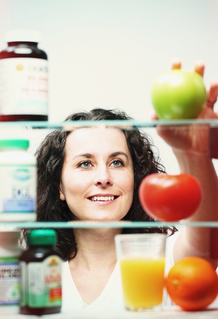 A woman choosing between vitamin tablets and fresh fruit and vegetables