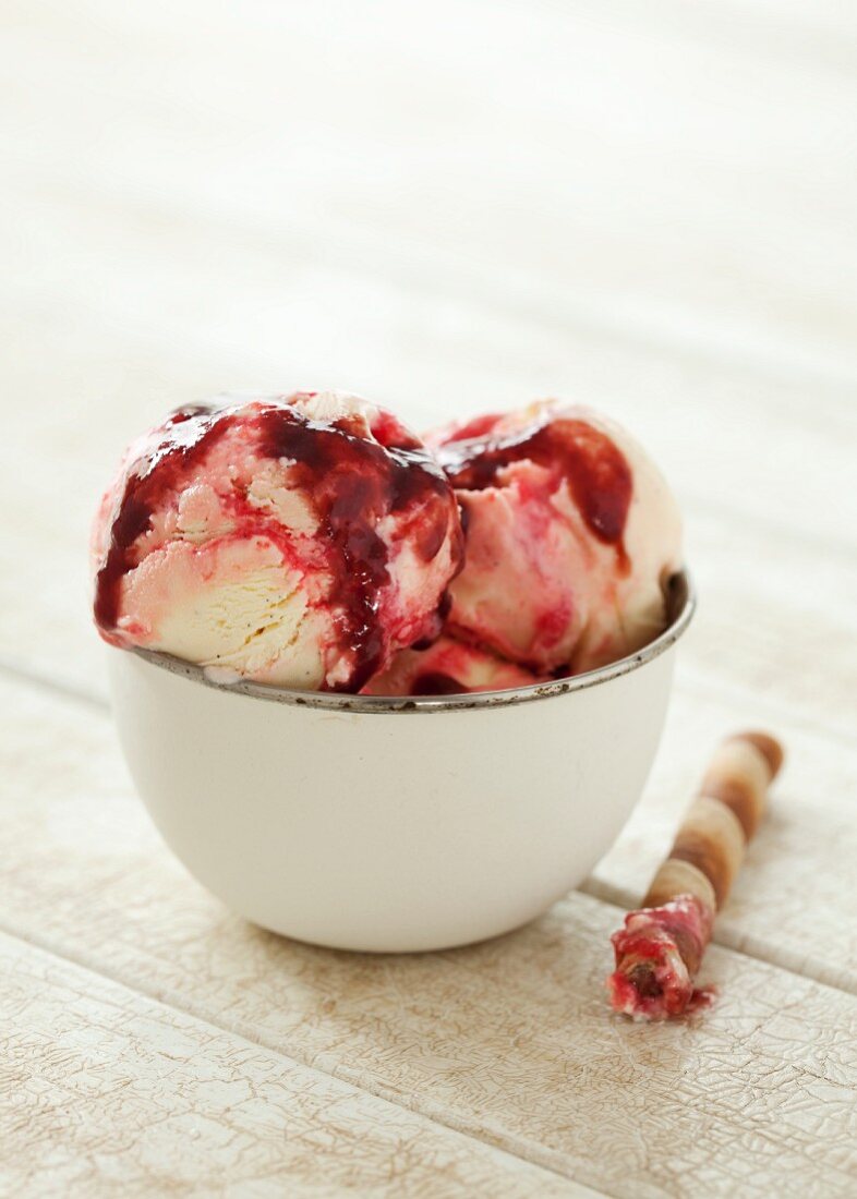 A bowl of icecream with raspberry sauce and a wafer cigar