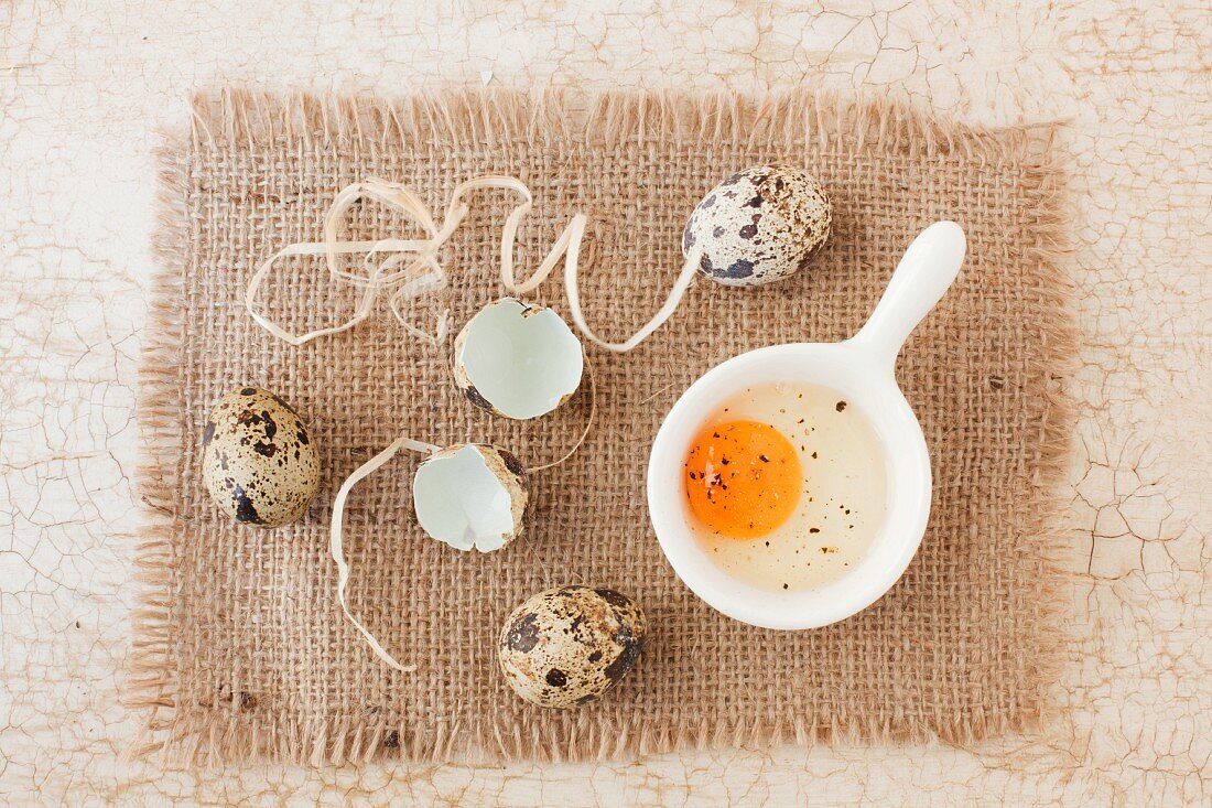 Three whole quail's eggs with a cracked open egg and shells