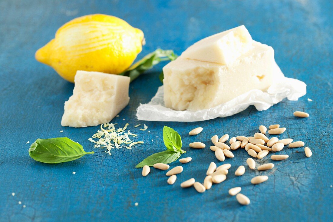 Pecorino cheese, basil, pine nuts and a lemon on a blue surface