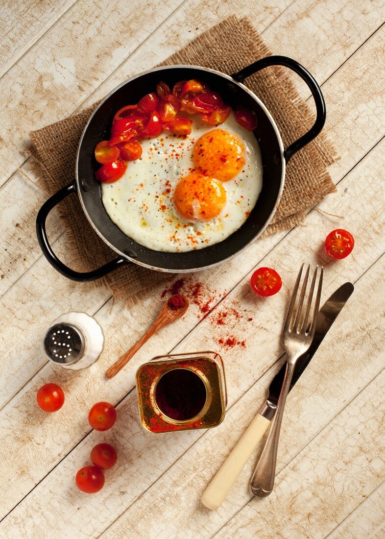 Two fried eggs and fried, chopped tomatoes sprinkled with paprika in a pan