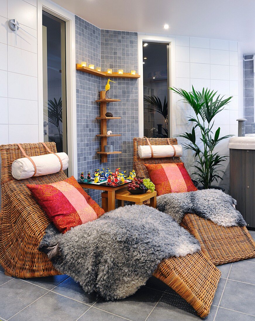 Rattan loungers with cushion and sheepskin blankets in spa bathroom with grey-tiled wall and floor