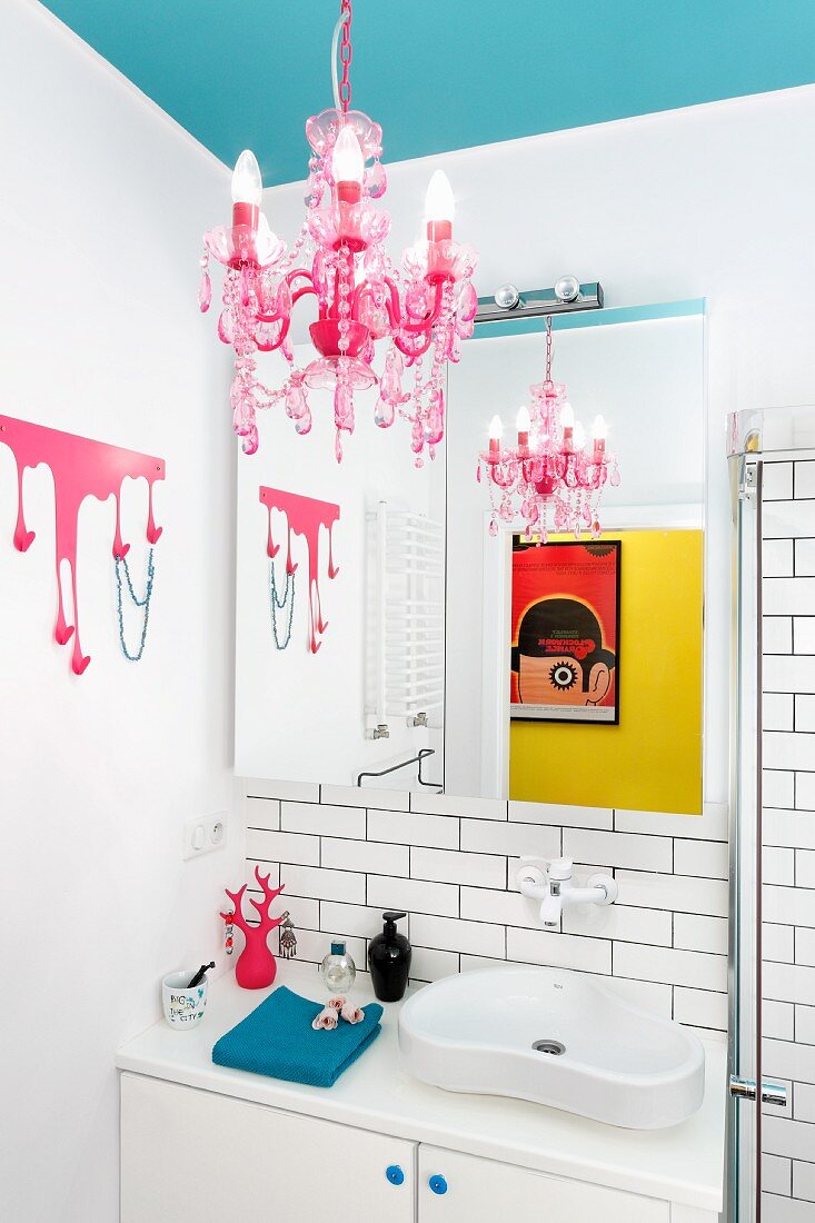 Pink chandelier suspended from light blue ceiling and organically shaped washbasin in feminine bathroom