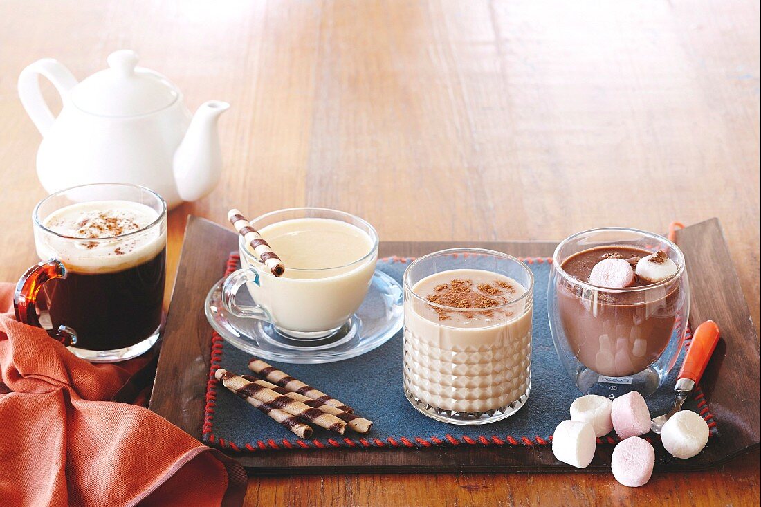 Five different hot drinks in glasses and jug on a wooden table