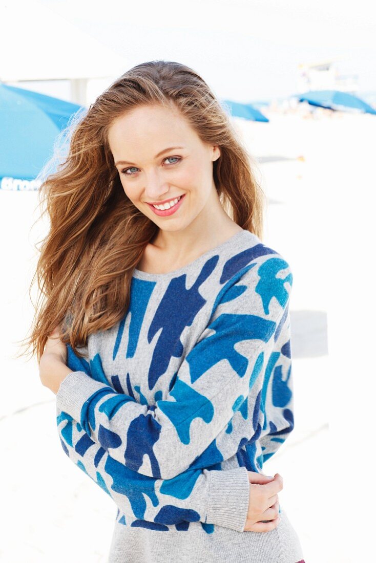 A young blonde woman on a beach wearing a blue patterned jumper