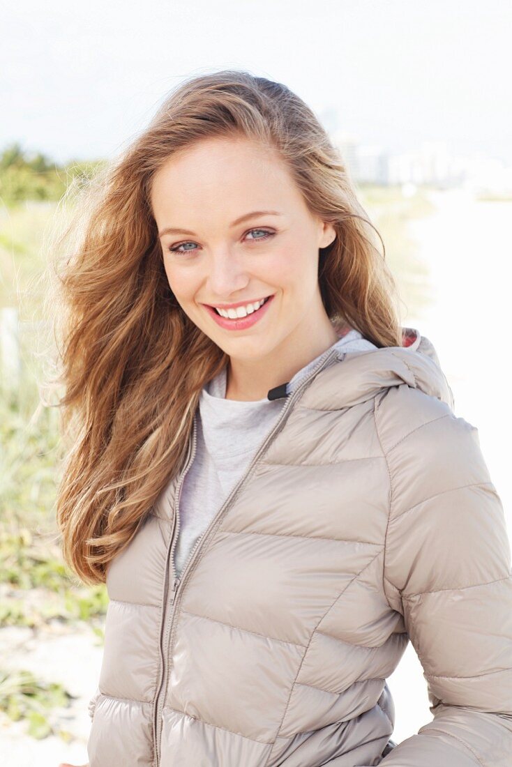 A young blonde woman outside wearing a beige quilted jacket