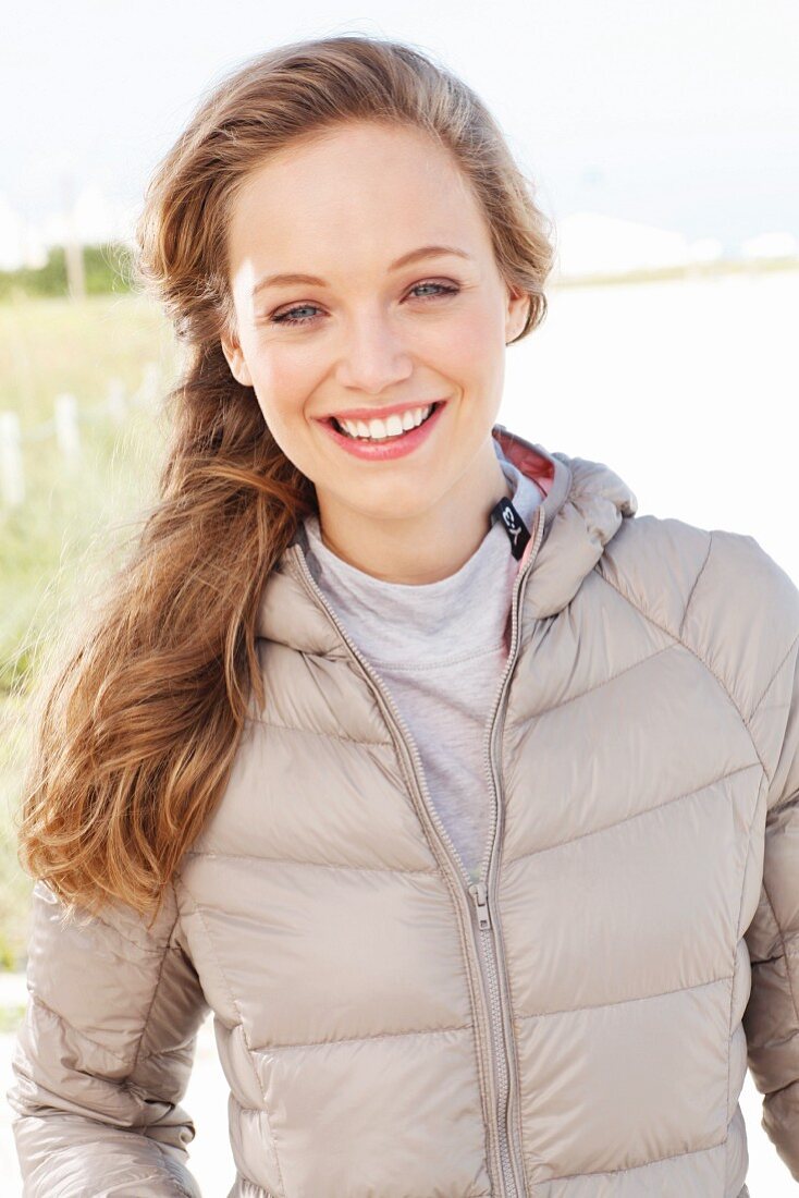 A young blonde woman outside wearing a beige quilted jacket