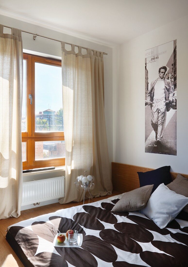 Bett mit Bettwäsche in modernem Dessin am Fenster mit bodenlangen Vorhängen