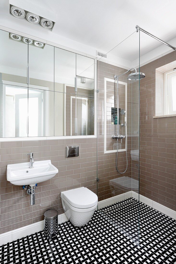 Designerbad mit eingebautem Spiegelschrank, seitlich bodenebener Duschbereich mit Glas Trennwand, auf Fliesenboden geometrisches Muster