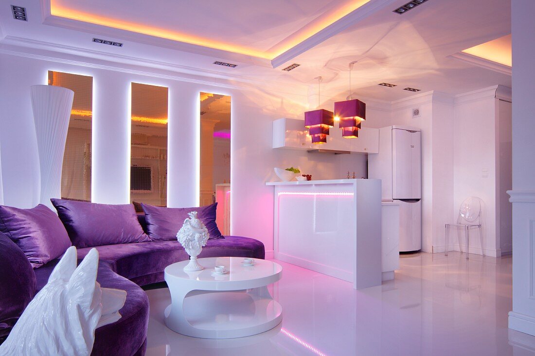 Purple sofa and white, round, designer coffee table in open-plan interior with atmospheric lighting