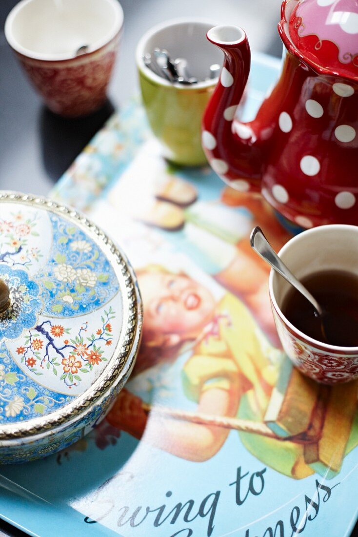 Verschiedene Becher, gepunktete, rote Kanne und chinesische Porzellandose auf Set mit Kindermotiv aus den Fifties