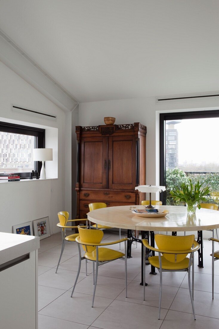 Yellow retro chairs at round table and antique cupboard in corner next to floor-to-ceiling window