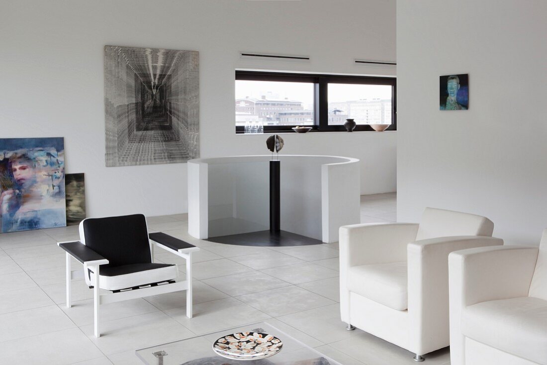 White, designer armchairs and black chair in minimalist lounge area; head of staircase with circular balustrade in background