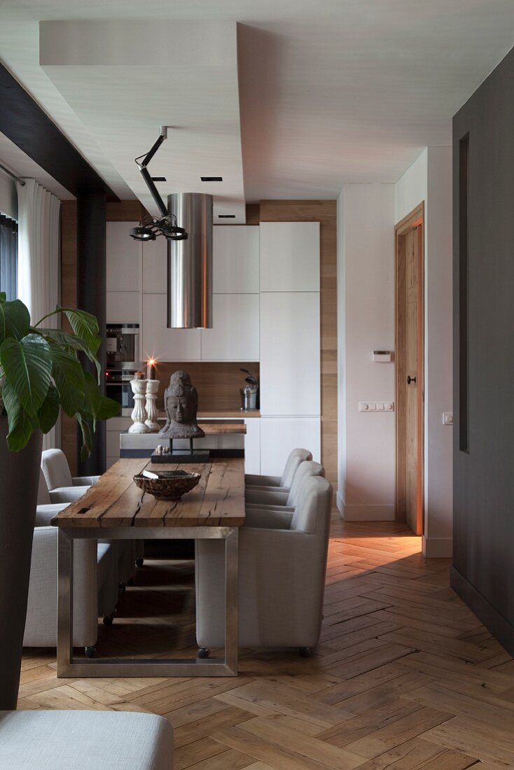 Dining set with armchairs at custom dining table and modern, white fitted kitchen in background