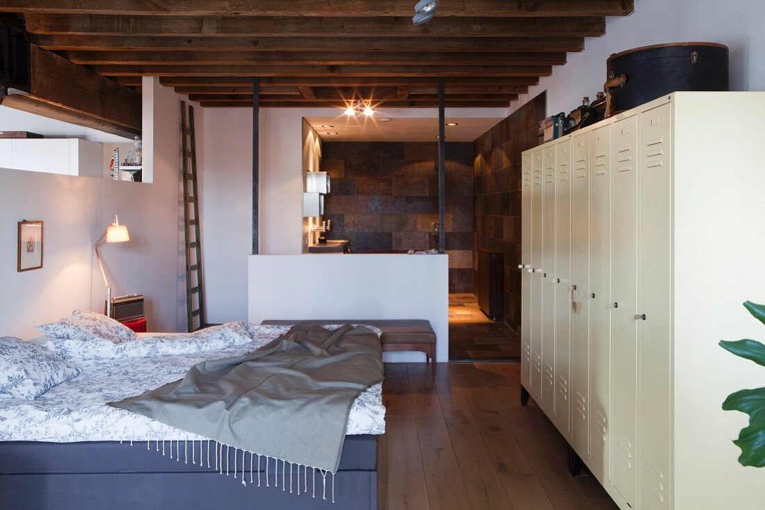 Bedroom with rustic, wood-beamed ceiling, white lockers and ensuite bathroom in loft apartment