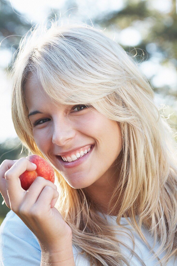 A smiling woman eating a peach
