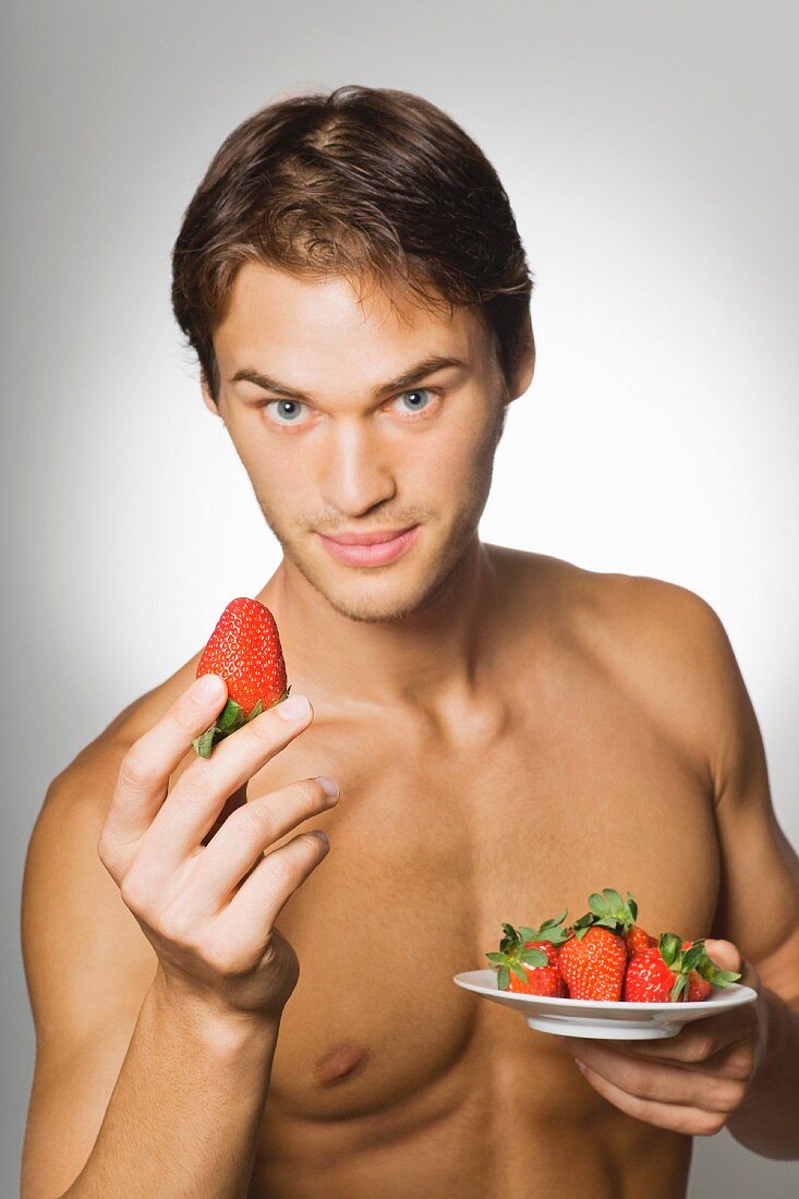 A young, topless man holding a large strawberry