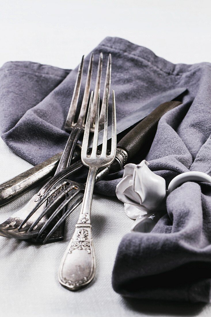 Old silver cutlery with a grey napkin on a white table cloth