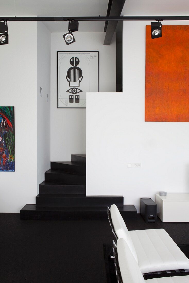 White leather armchair on black floor, winding staircase and track lighting system with spotlights