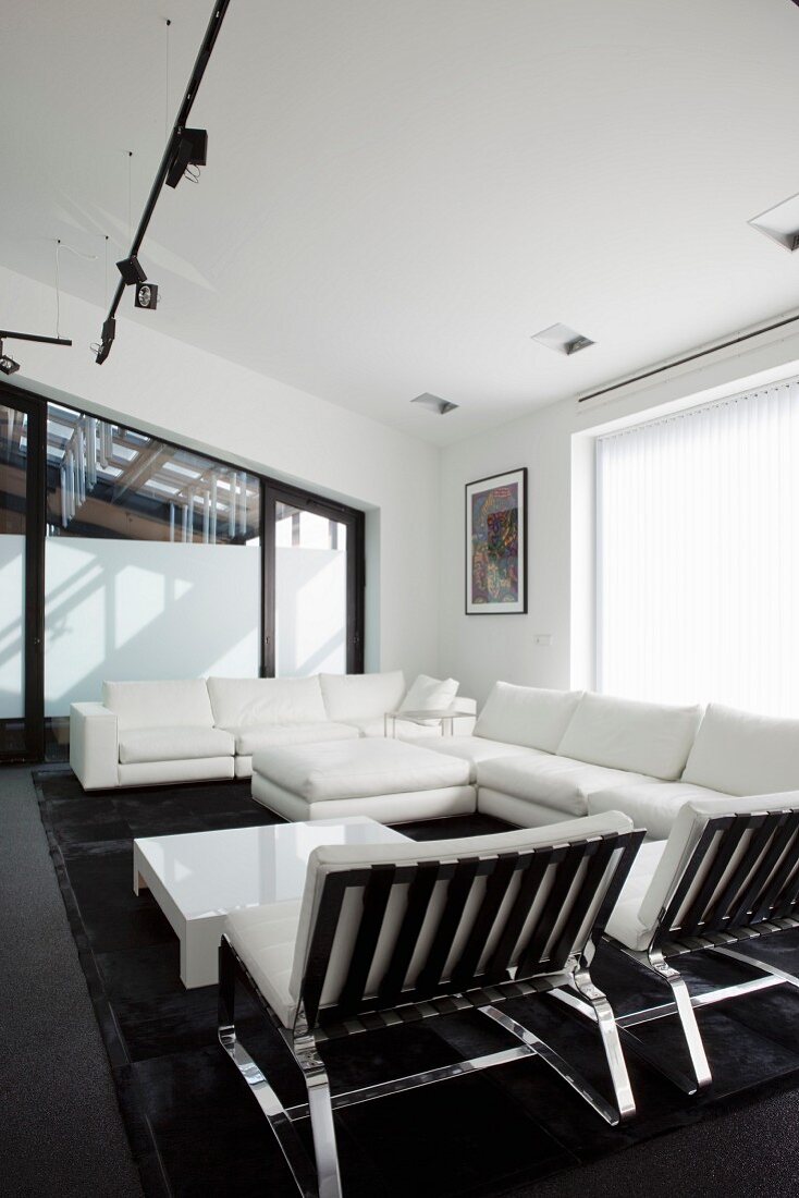 weiße Lounge Sitzmöbel um Bodentisch, an Decke schwarzes Lichtschienensystem mit Strahlern