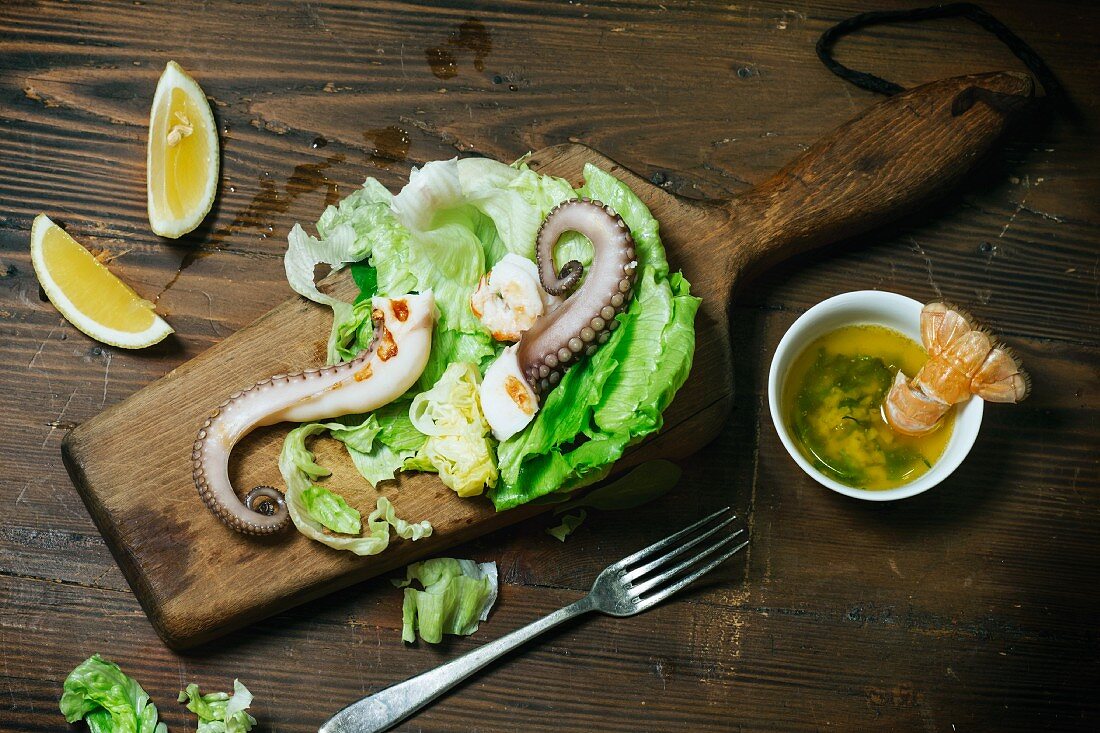 Grüner Salat mit gegrilltem Oktopus und Shrimps auf Holzbrett