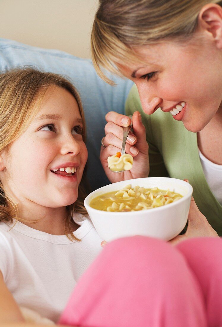 A mother and daughter eating chicken noodle soup