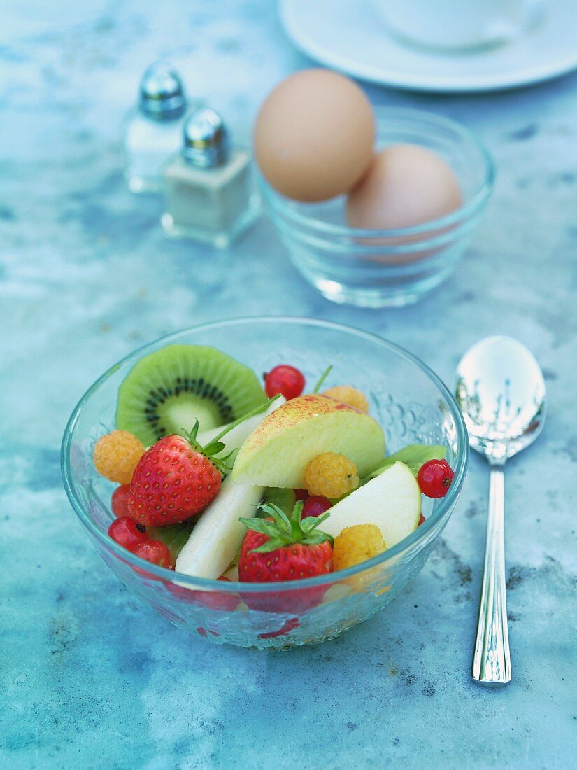 Fruit salad, eggs, salt and pepper on a breakfast table