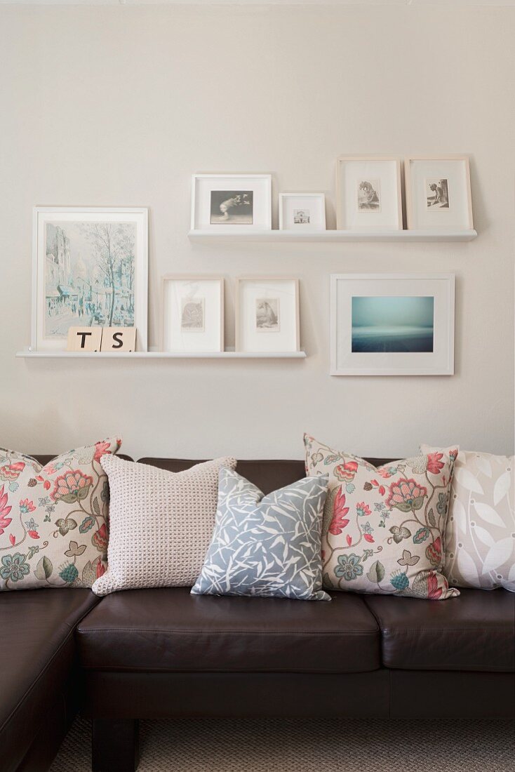 Floral scatter cushions on dark brown leather sofa and gallery of pictures in delicate shades on wall