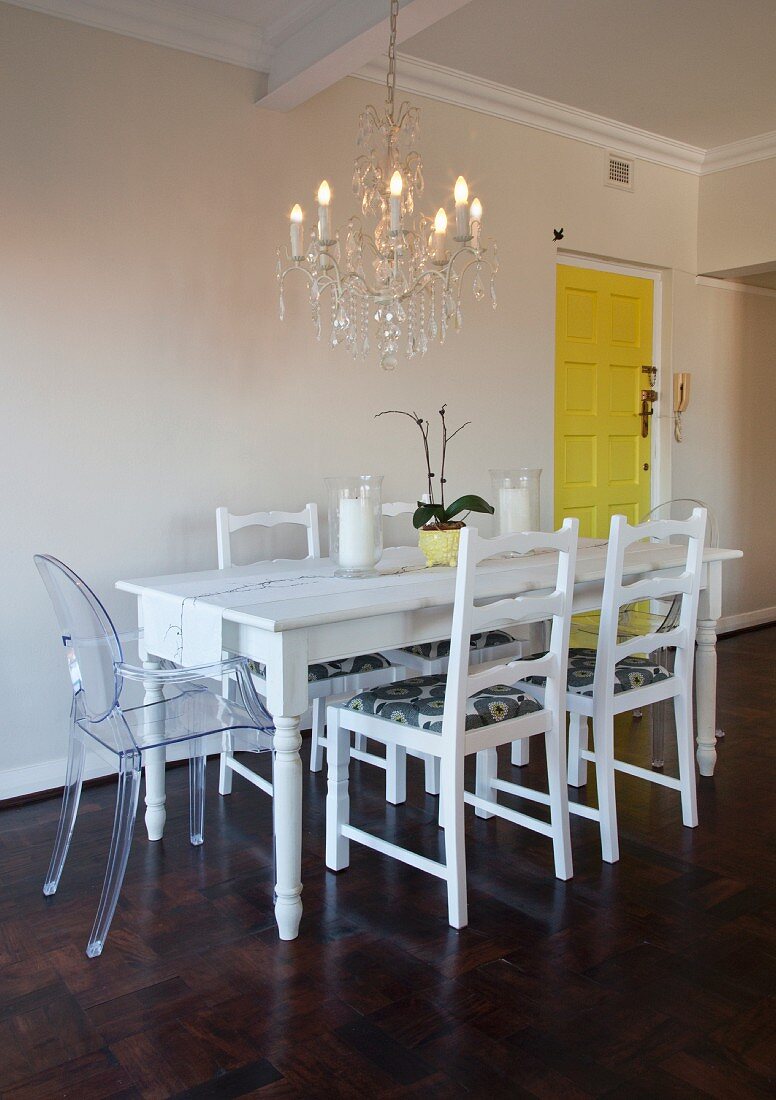 White dining table, refurbished second-hand chairs and Ghost chair below chandelier
