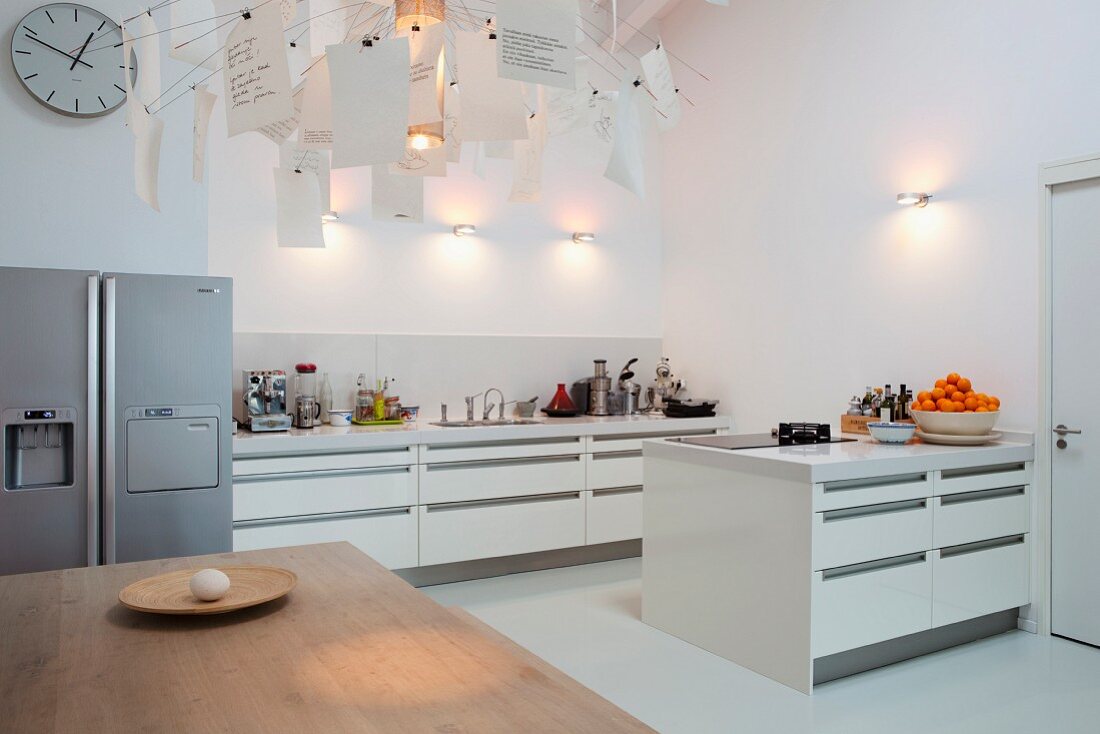 View across dining table into open-plan, white designer kitchen with stainless steel side-by-side fridge freezer