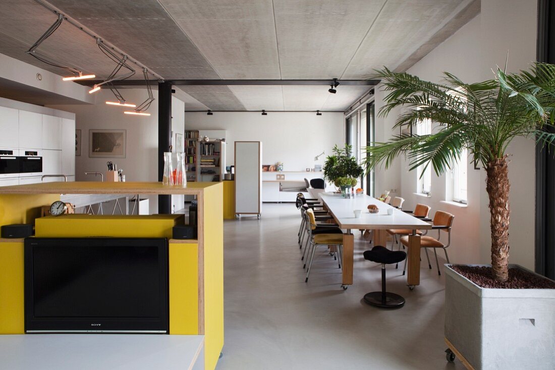 Yellow kitchen counter, long dining table and chairs in loft apartment