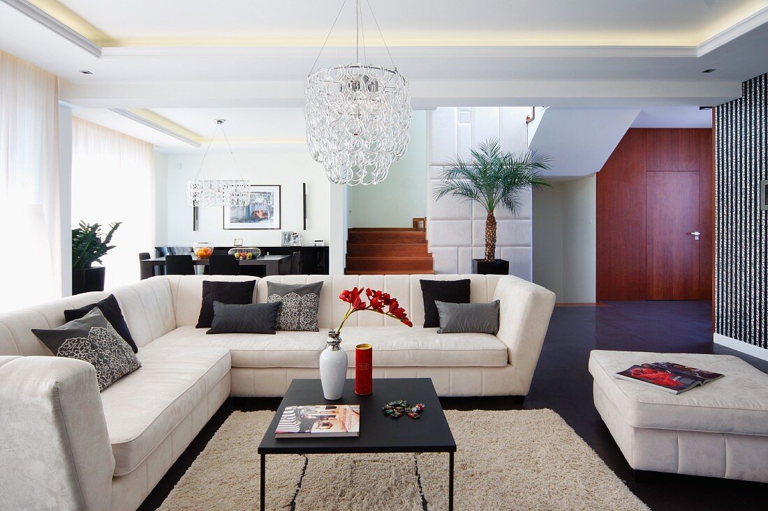 Elegante, helle Couch übereck und Couchtisch auf flokatiartigem Teppich in offenem Wohnraum mit indirekter Deckenbeleuchtung