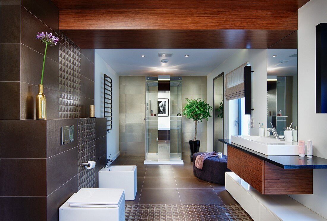 Elegantes Designerbad - Massgefertigter Waschtisch, gegenüber Sanitärmöbel an braun gefliester Wand, im Hintergrund Duschbereich