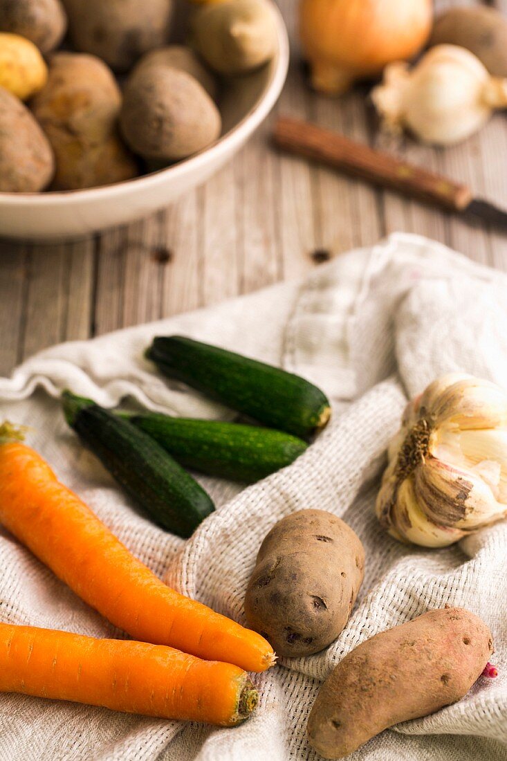 Gemüsestillleben mit Möhren, Kartoffeln, Knoblauch und Zucchini auf Geschirrtuch