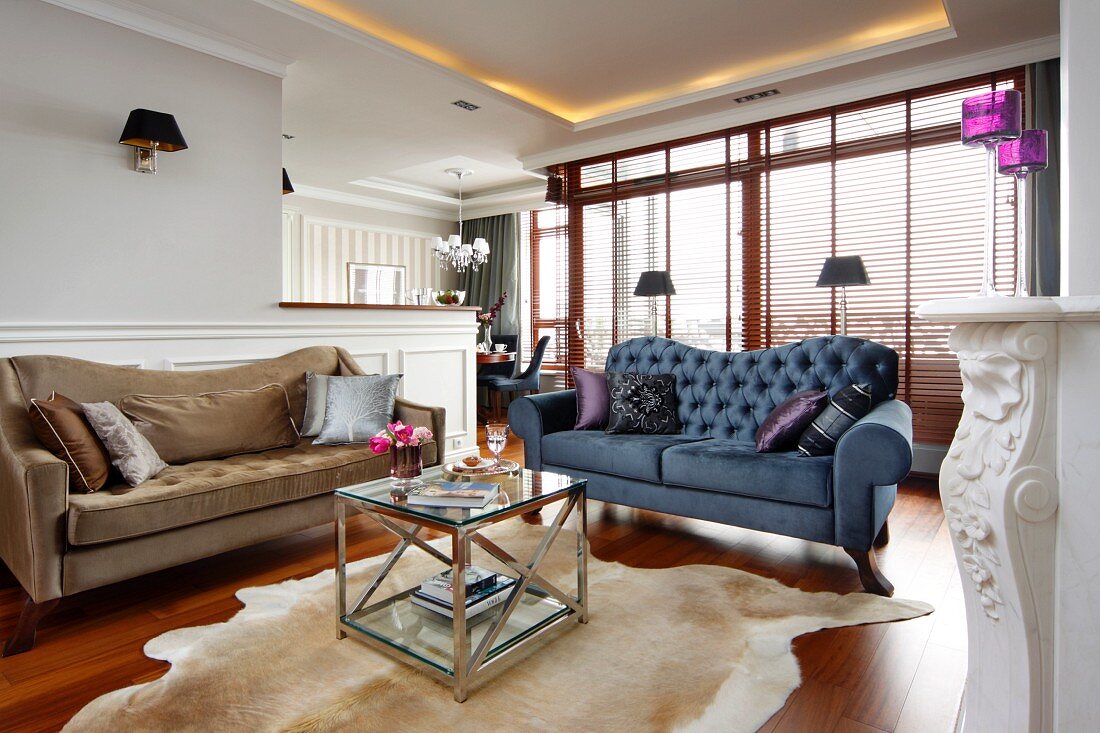 Beige and blue sofas around coffee table on animal-skin rug in traditional fireplace with indirect ceiling lighting