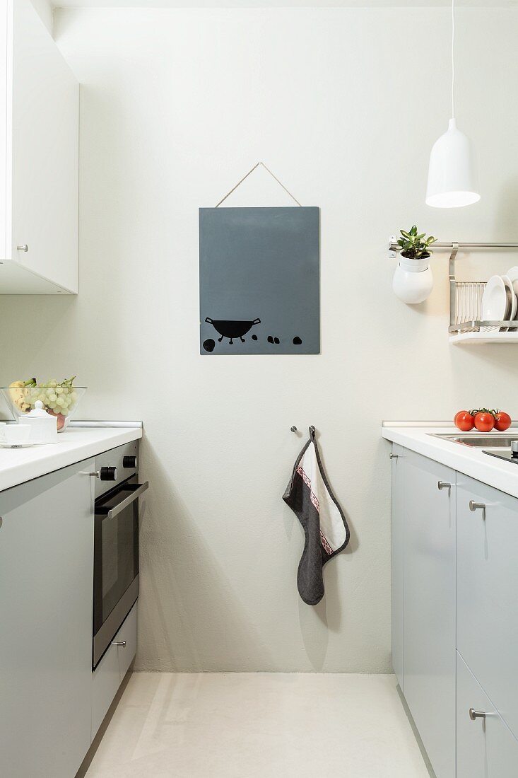 Two opposite, pale grey kitchen counters, tea towel hung on hook and picture on wall