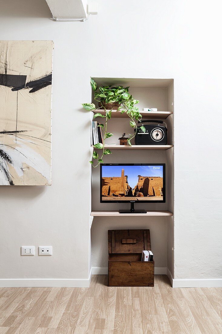 Eingebaute Regalbretter in weiße Wandnische mit Holztruhe, Flachbildschirm, Retroradio und Grünpflanze dekoriert