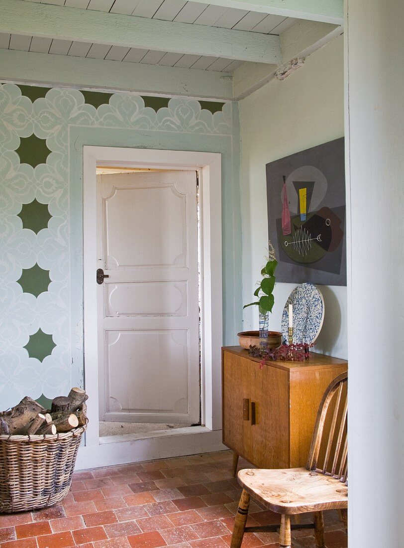 Basket of firewood next to interior door with chair and cabinet to one side on terracotta floor