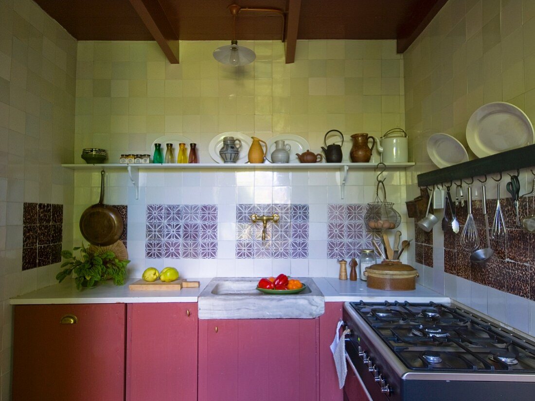 Küchenzeile mit altrosa Unterschränken vor gefliester Wand, oberhalb Kannen auf Ablage