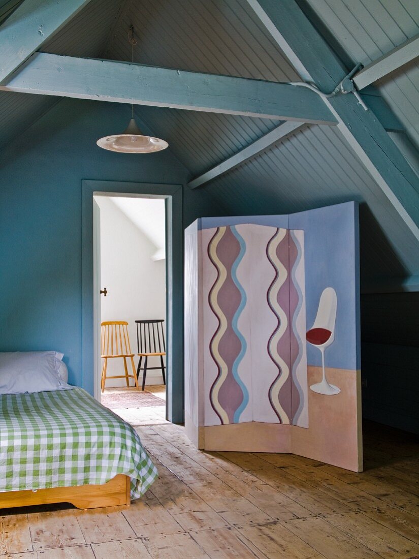 Bemalter Paravent neben Bett, im Hintergrund offene Tür und Blick auf Stühle, in ausgebautem Dachgeschoss mit blaugrau gestrichener Holzverkleidung