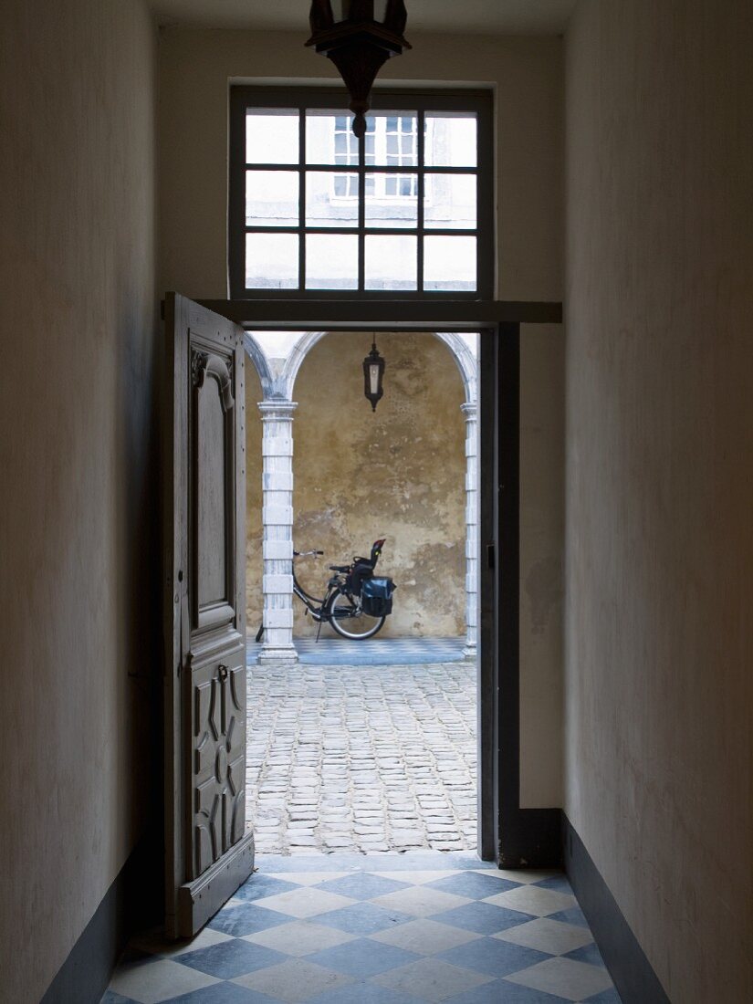 Open, historical front door with diamond-chequered floor tiles and view into cobbled courtyard