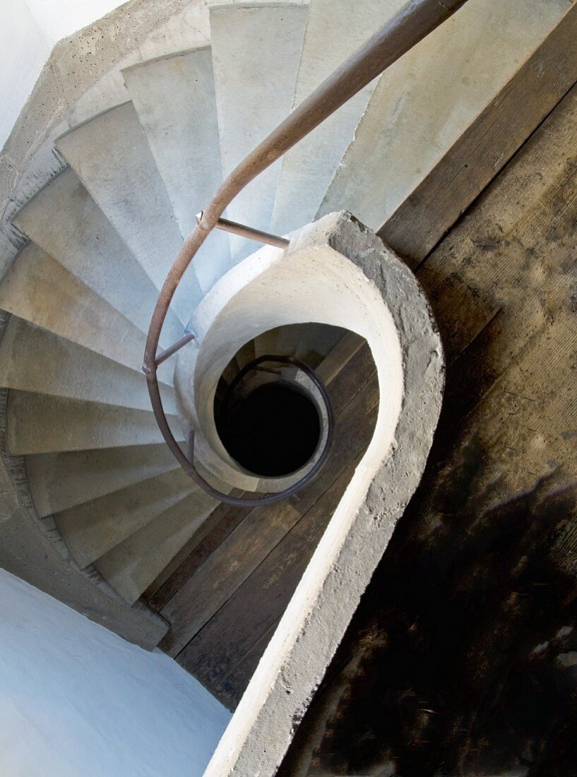 Blick von oben ins Treppenauge mit schneckenförmigem Geländer und gewendelte Treppe aus Beton
