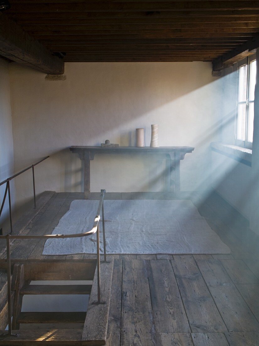 Beams of sunlight slanting through windows onto restored gallery with rustic wooden floor and antique console table
