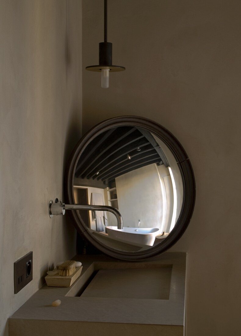 Minimalist sink with wall-mounted tap and bathtub reflected in round mirror