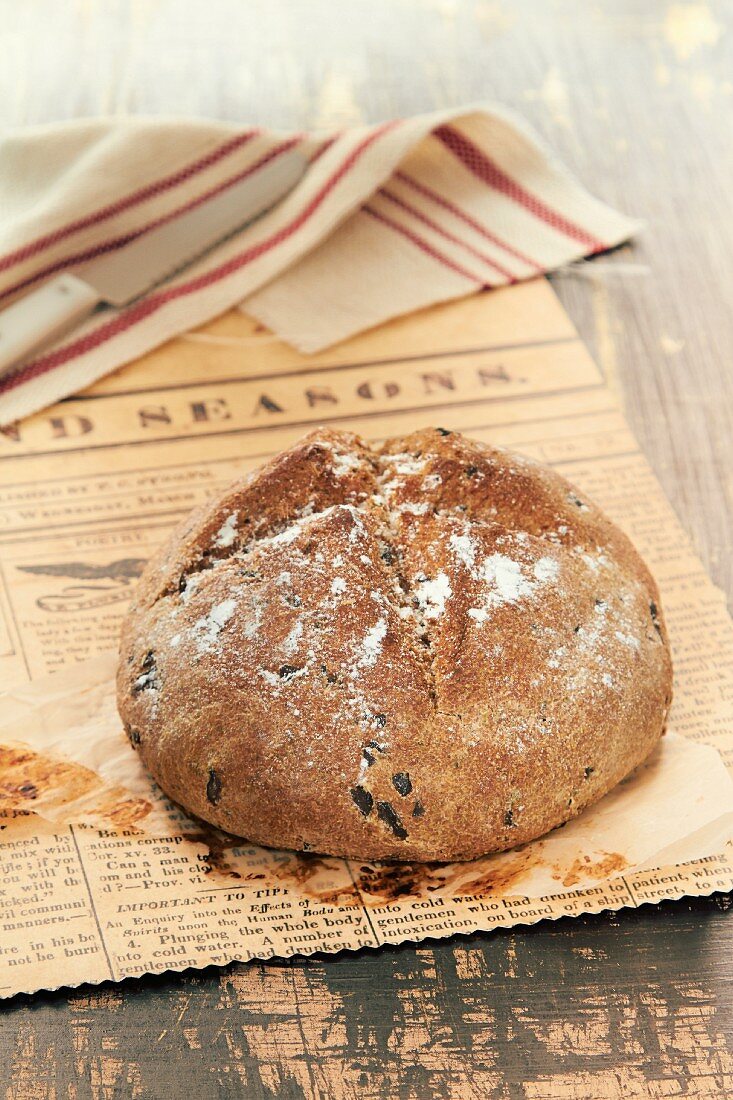 A loaf of olive bread on a piece of newspaper
