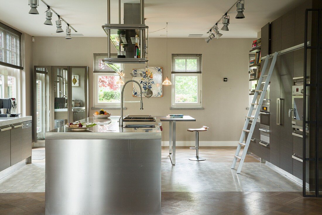 Stainless steel island counter below extractor hood in designer kitchen with fitted cupboards