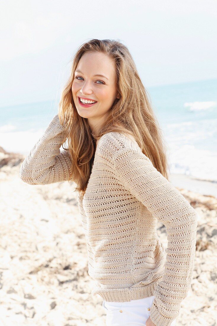 A happy young on a beach wearing a crocheted jumper