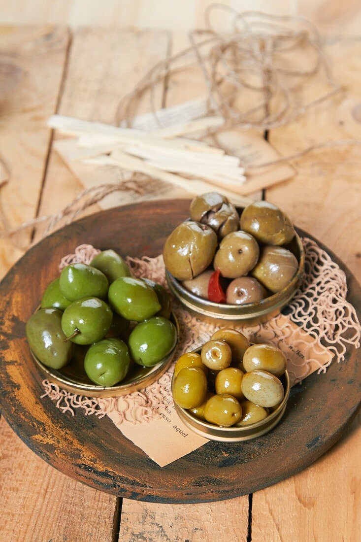 Verschieden gewürzte, grüne Oliven in drei Metalldeckel