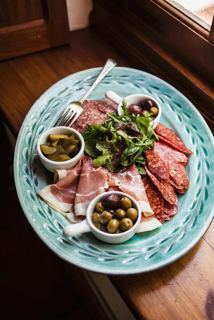 A meat platter with bacon, olives and gherkins